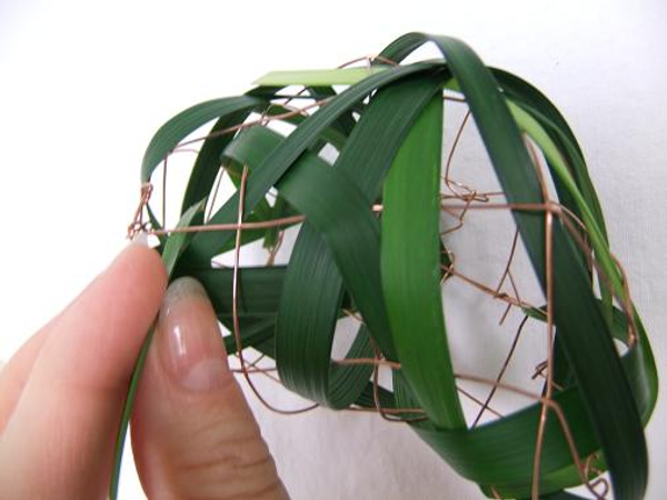 Use the thicker side of the blade of grass to thread it through the wire mesh.
