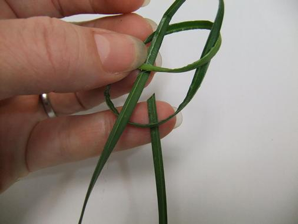 Bend the blade of flax and weave it under the outside loop of the knot