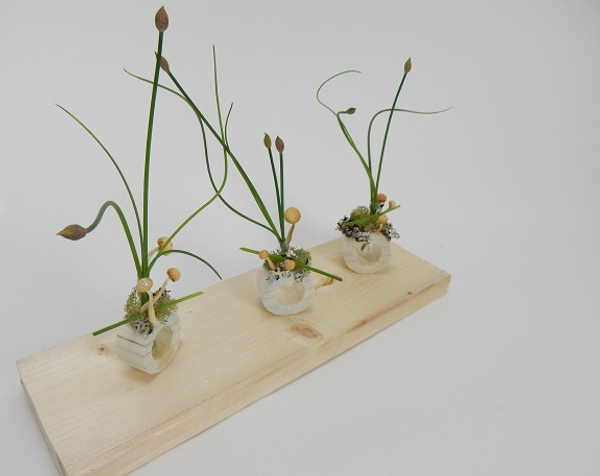 Chive flower heads with moss lichen and mushrooms in a dowel stick container