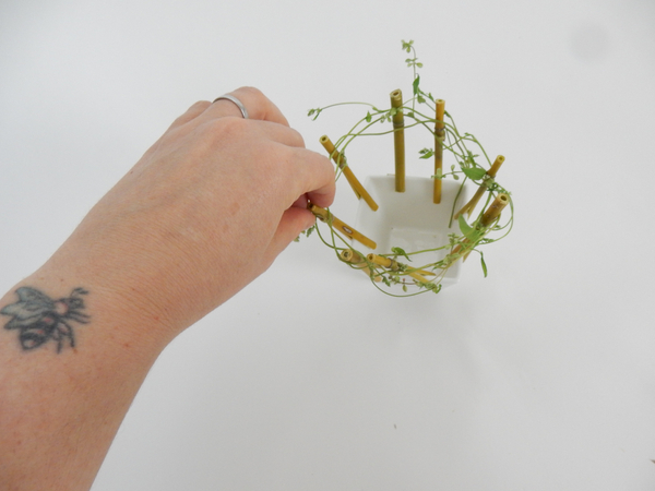 Continue to weave the vine through the bamboo and set the end of the stem in the container