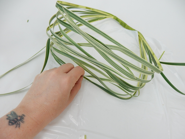 Fold the blades of grass over and secure it to the bottom of the basket, one strand at a time