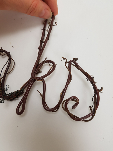 Carefully open a few vine tendrils and curl it around the letters