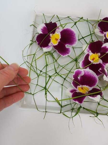 Set your flowers in the shallow container.  The flower stems should be in water and the flower resting above the water on the knotted net of ripped grass.