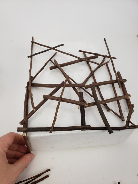 Start to glue twigs to the bottom edge of the shape