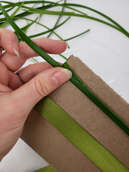 Wrap the grass strand around the cardboard in the same direction as the ribbon.