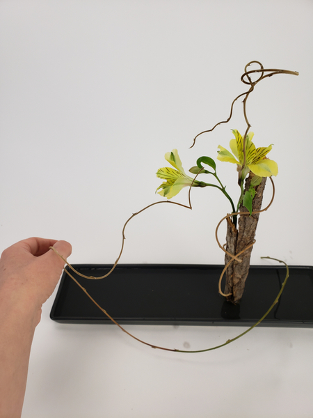 Carefully manipulate the vines to wind around the bark log and flowers to create a focal point