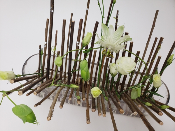 Stack twigs in a long container as an armature to display a few flower buds