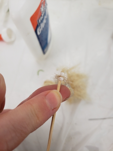 Take a tiny drop of wood glue on the end of a bamboo skewer and place the string in the glue letting the bells dangle down