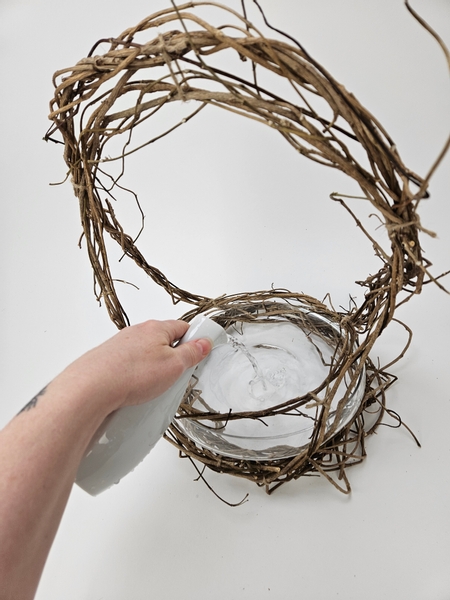 Pour water into the shallow container in the wreath basket