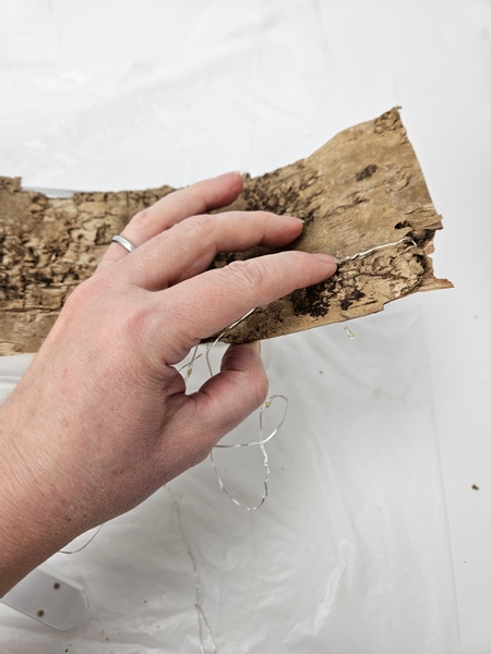 Catch the end of the fairy lights on the bark strip so that they hook into position securely