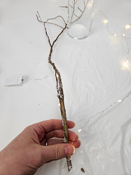 Place the battery pack of a string of fairy lights at about the middle of the twig