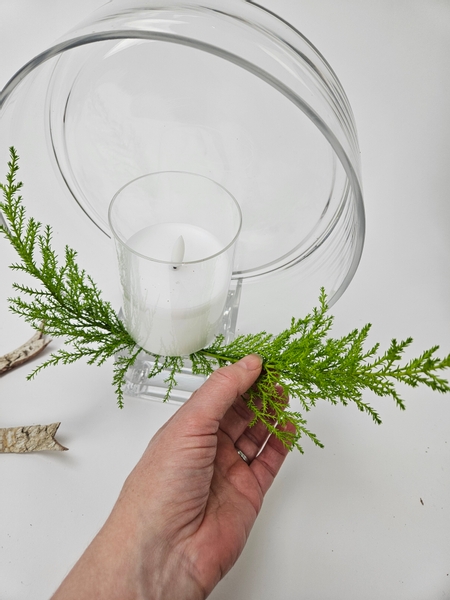 Slip two cypress branches under the candle and into the water in the container below